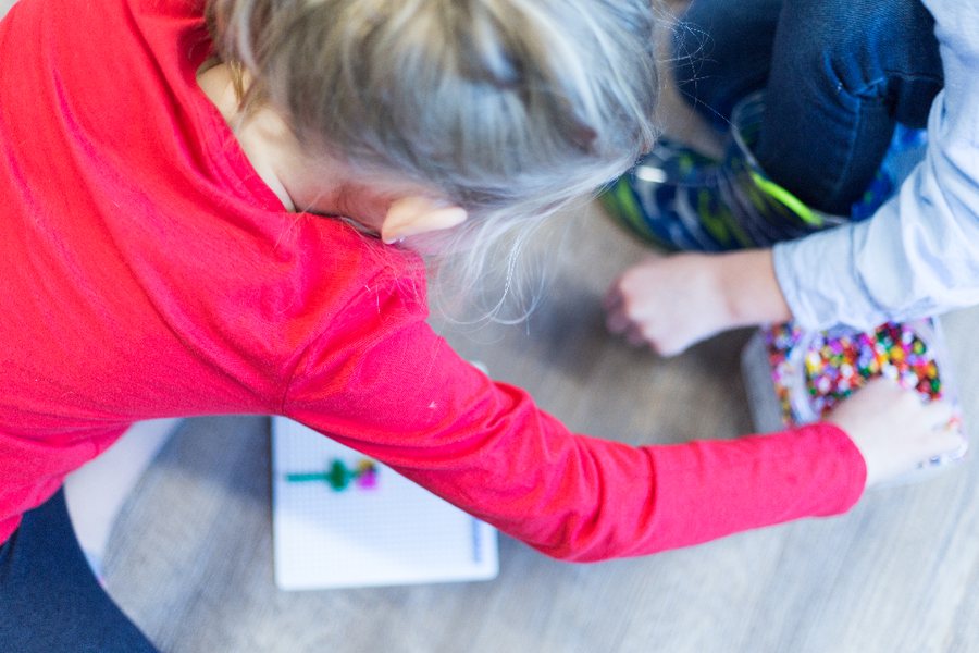 Enfant qui enfile des perles avec un adulte, une activité calme avant un bilan neuropsychologique