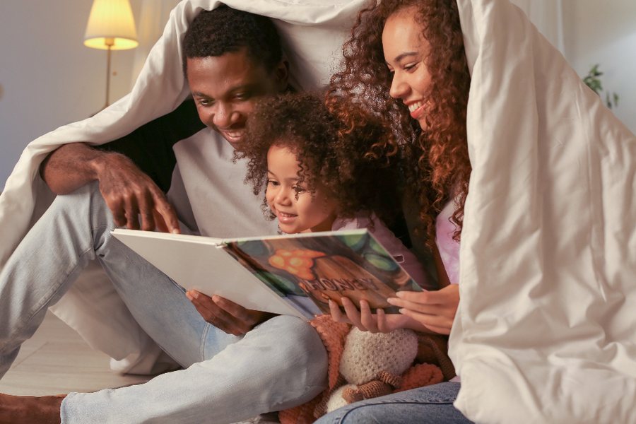 Parents et enfant réunis sous une couverture autour d'un livre : décrire le quotidien de l'enfant pour le dossier MDPH