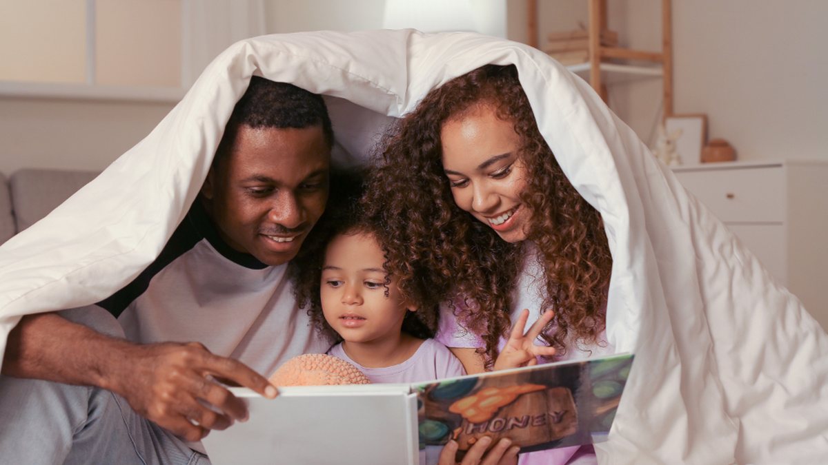 Parents et enfant qui lisent ensemble sous une couverture : repérer les signes d'un enfant HPI