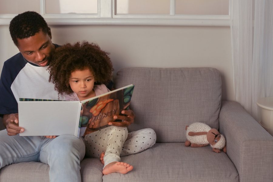 Père et fille installés sur le canapé avec un livre : un moment calme plutôt qu'une punition pour un enfant TDAH